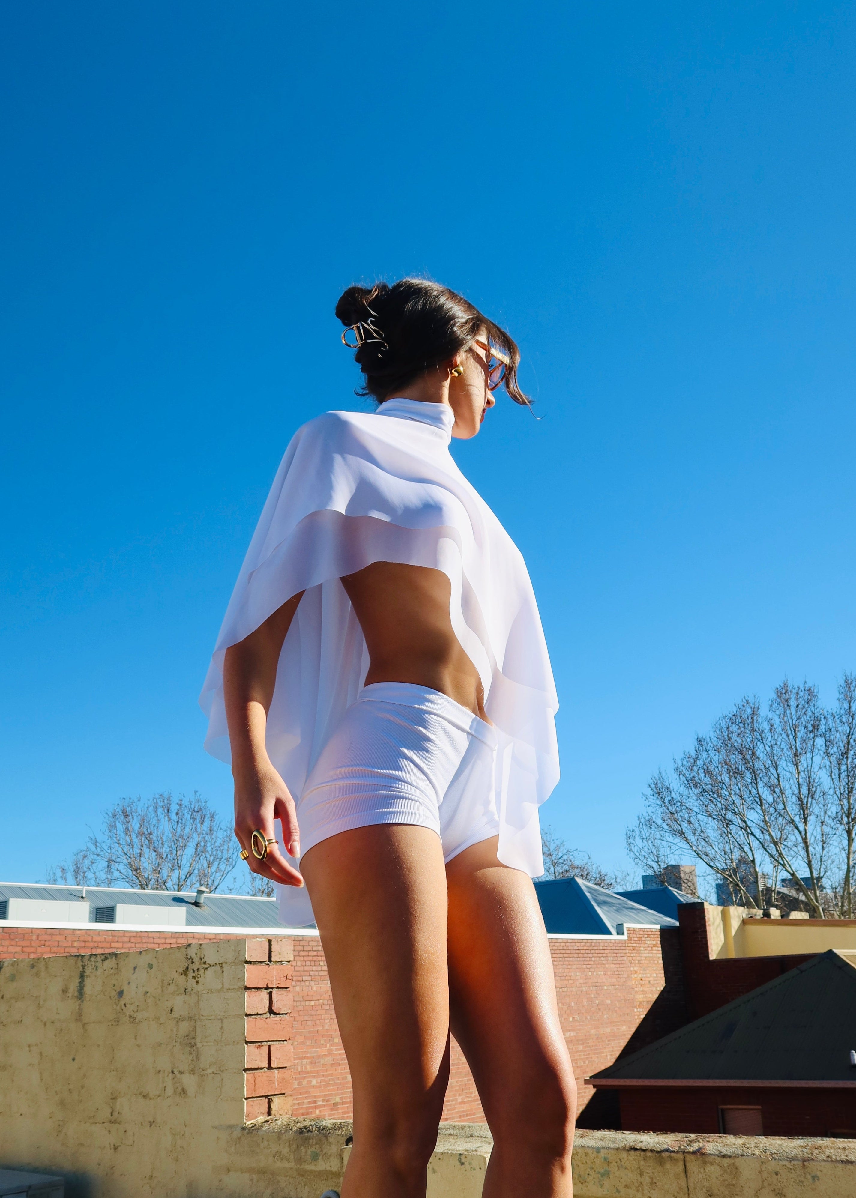Person wearing a white shirt and shorts on a rooftop with a clear blue sky.