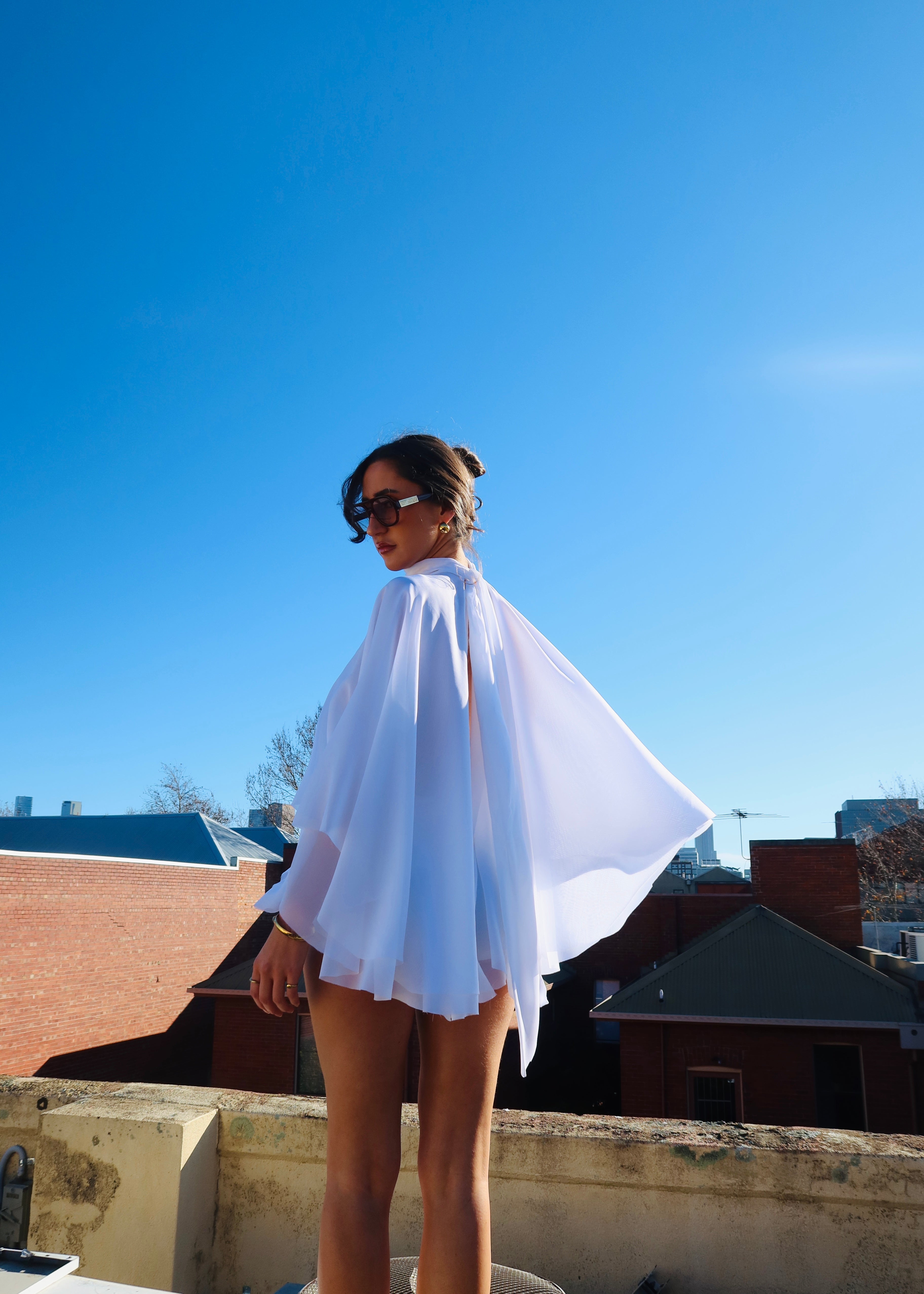 Person wearing a white cape on a rooftop with clear blue sky